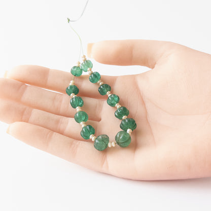 A person holds delicate pieces of Beryl and Shell Pearl beads, showcasing their pumpkin cut design.