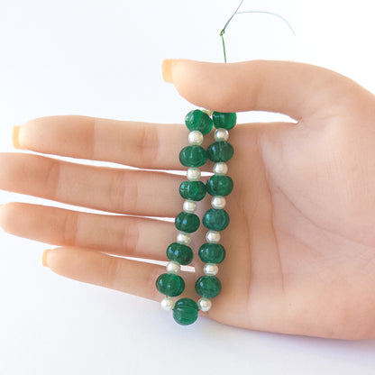 A person holds delicate strands of Beryl and Shell Pearl beads, showcasing their pumpkin‑cut design.