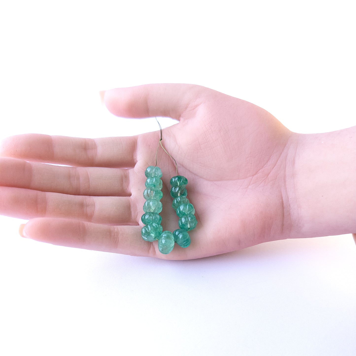A person holds delicate strands of Beryl beads, showcasing their pumpkin‑cut design.