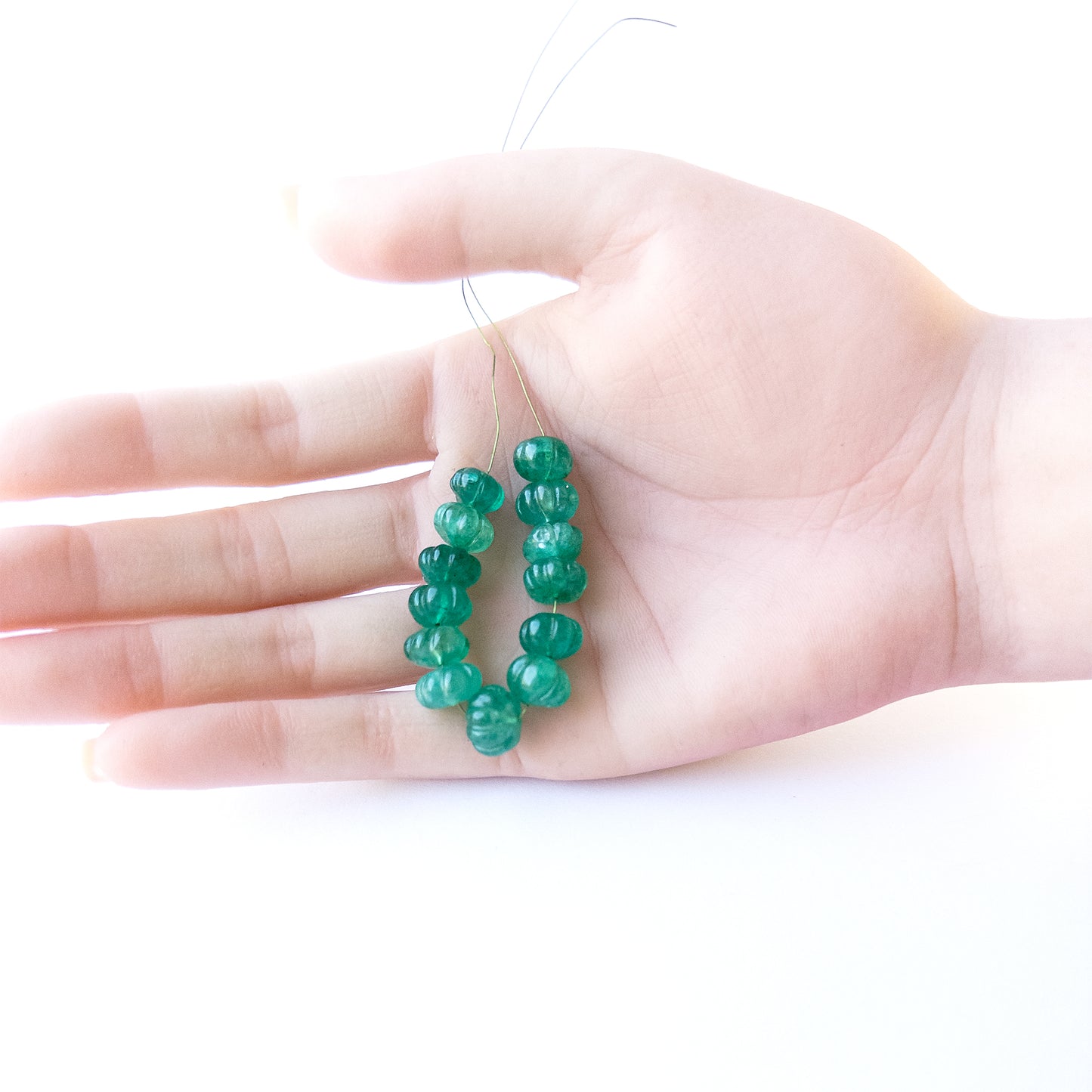 A person holds delicate strands of Beryl beads, showcasing their pumpkin‑cut design.