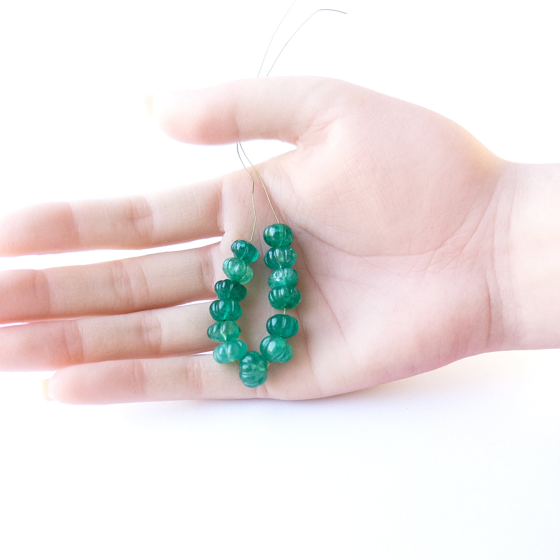 A person holds delicate strands of Beryl beads, showcasing their pumpkin‑cut design.