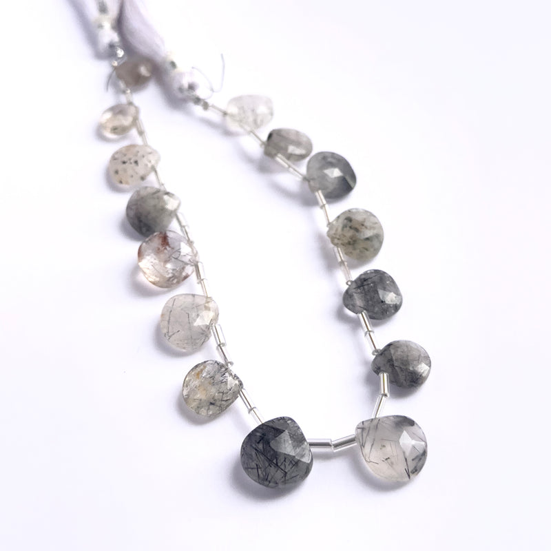 Close-up of natural gemstone beads showing the faceted briolette cut and rutile needle patterns.