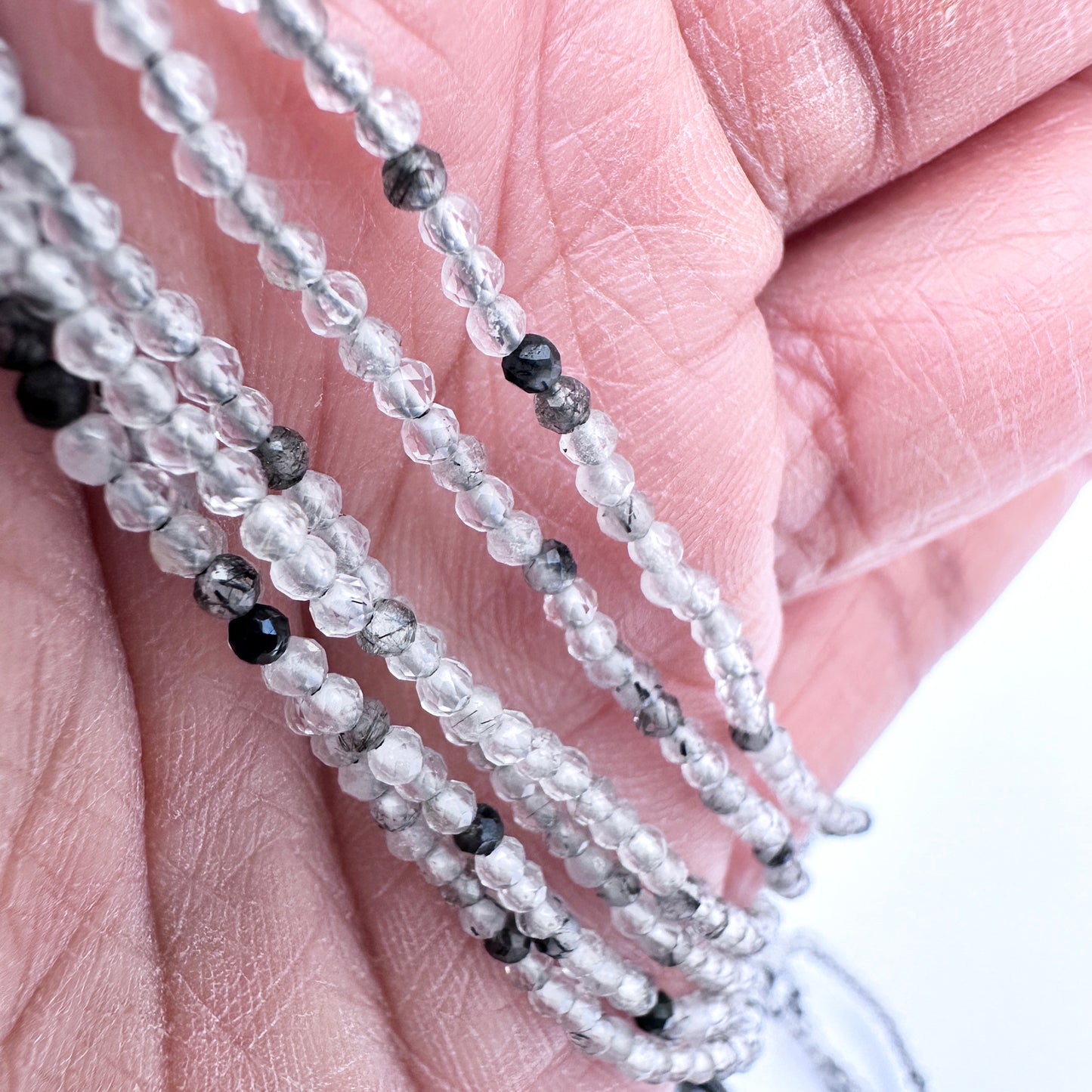 A person holds delicate strands of black rutile beads, showcasing their smooth design.