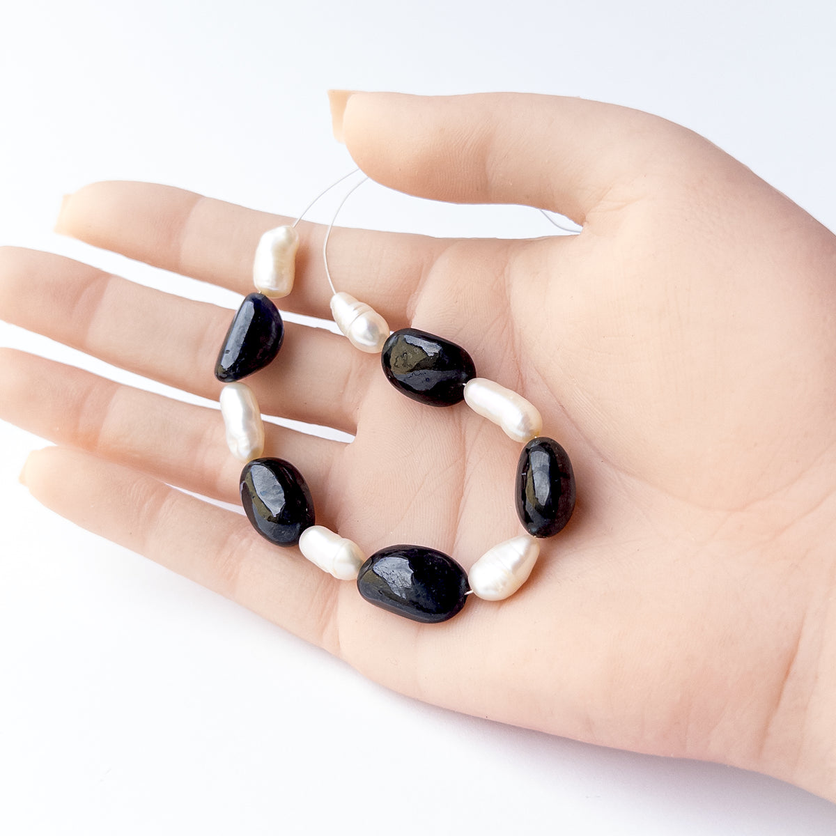 A person holds delicate pieces of Black Sapphire and Freshwater Pearl beads, showcasing their smooth tumble design.