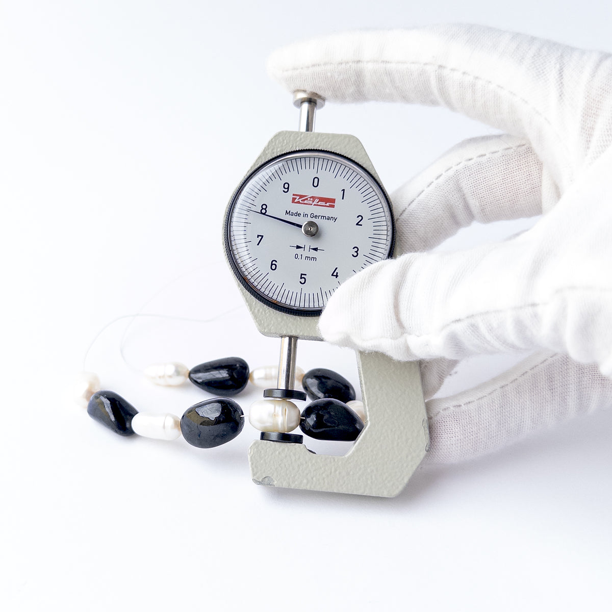A coin is place near delicate pieces of Black Sapphire and Freshwater Pearl beads for scale.