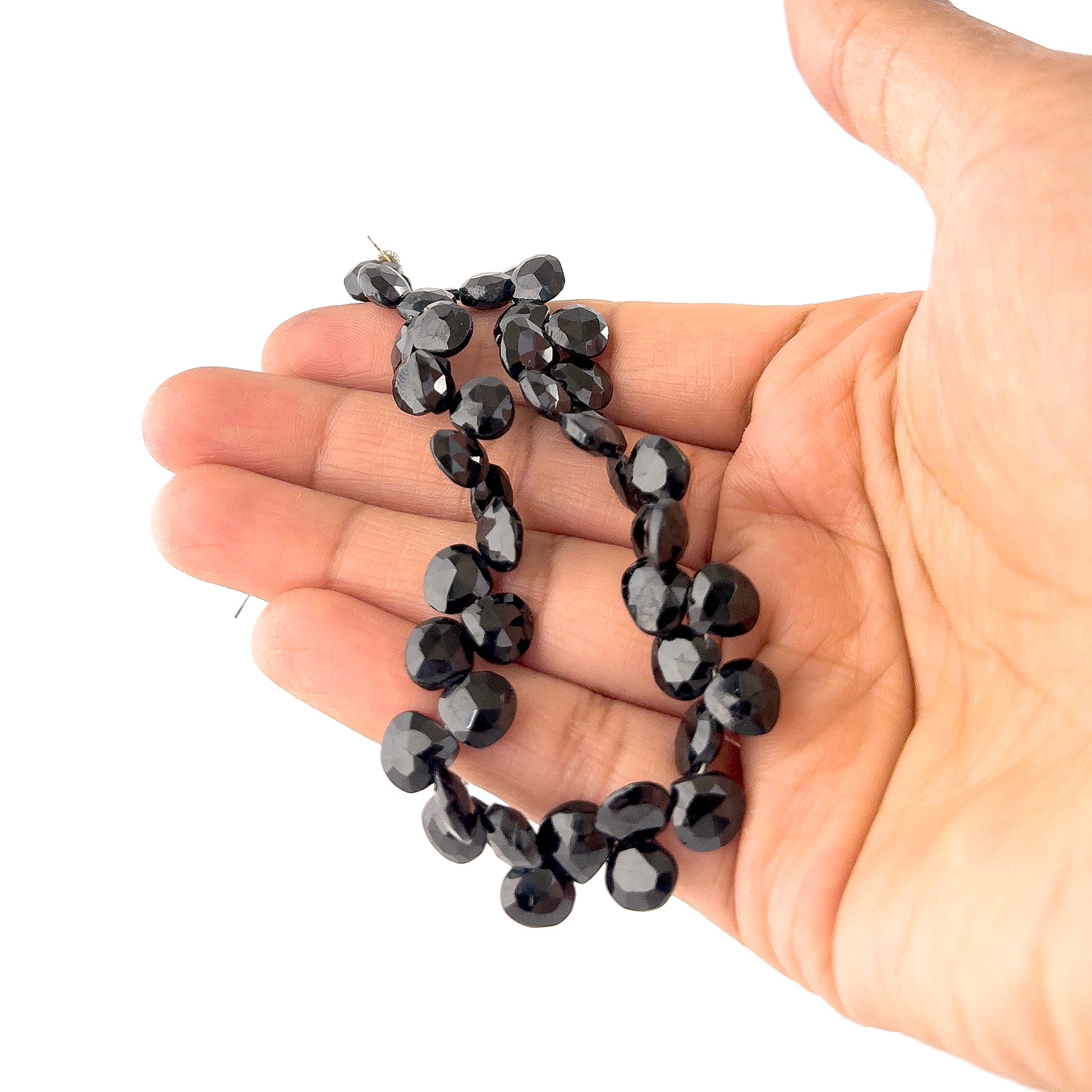 A person holds Black Spinel briolette beads, showing their faceted teardrop design and glossy black finish.