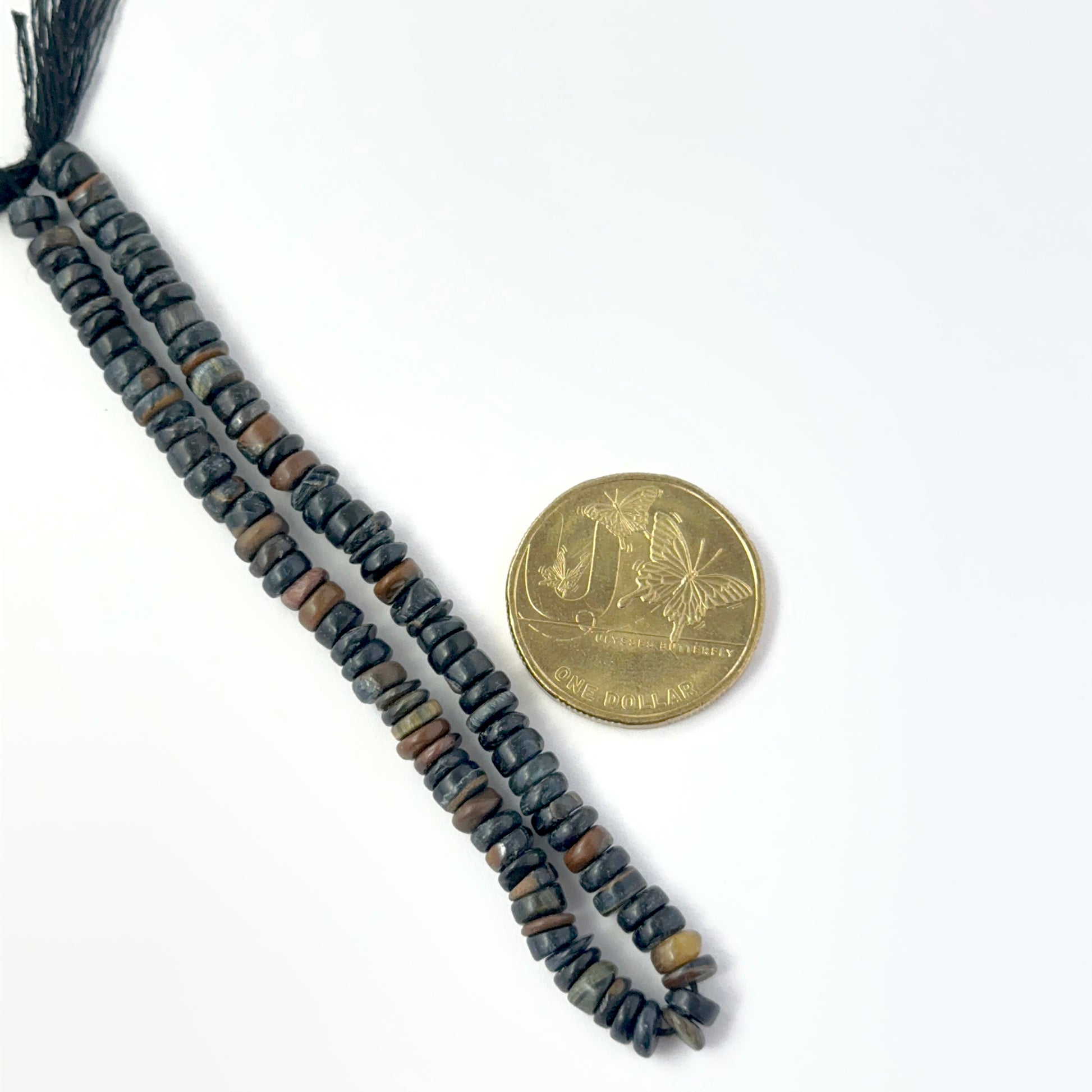 A coin is placed near delicate strands of Tiger Eye beads for scale.