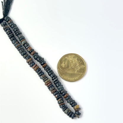 A coin is placed near delicate strands of Tiger Eye beads for scale.