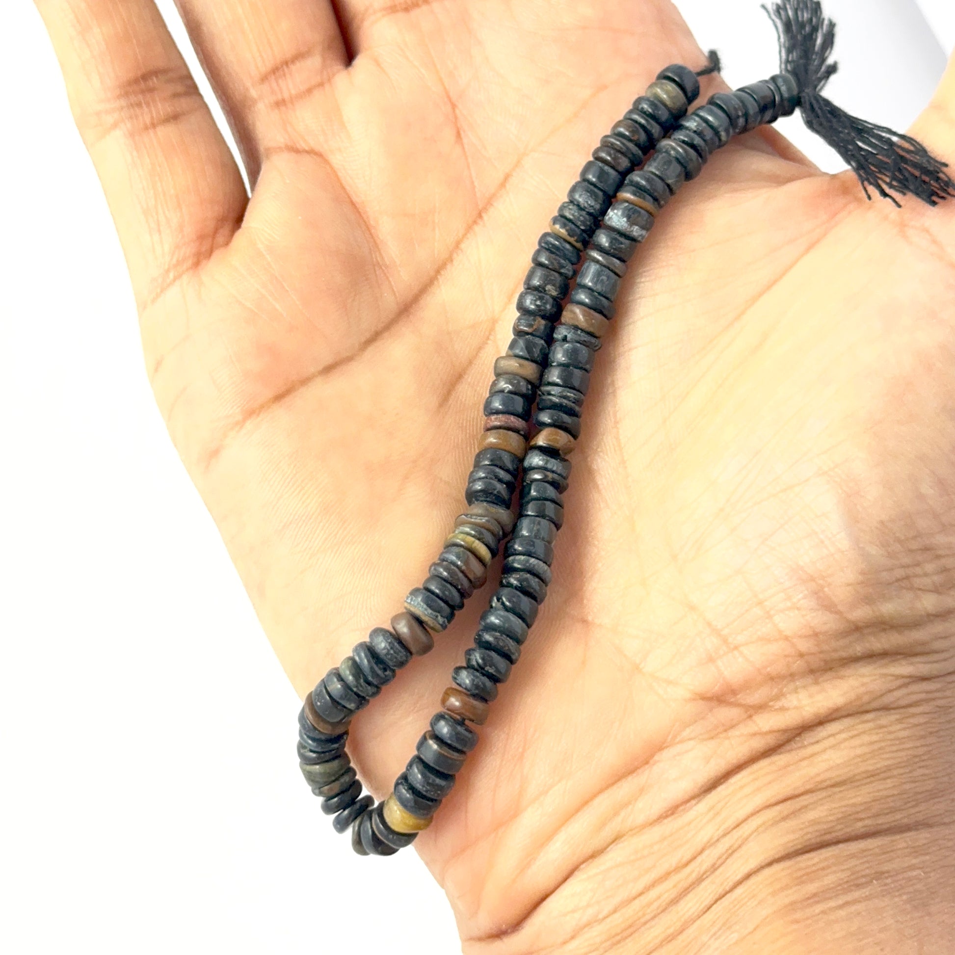 A person holds delicate strands of Tiger Eye beads, showcasing their smooth wheel design.