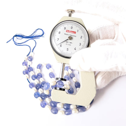 A dial gauge measures the Blue Quartz and Shell Pearl smooth oval 6–7.5mm gemstone.