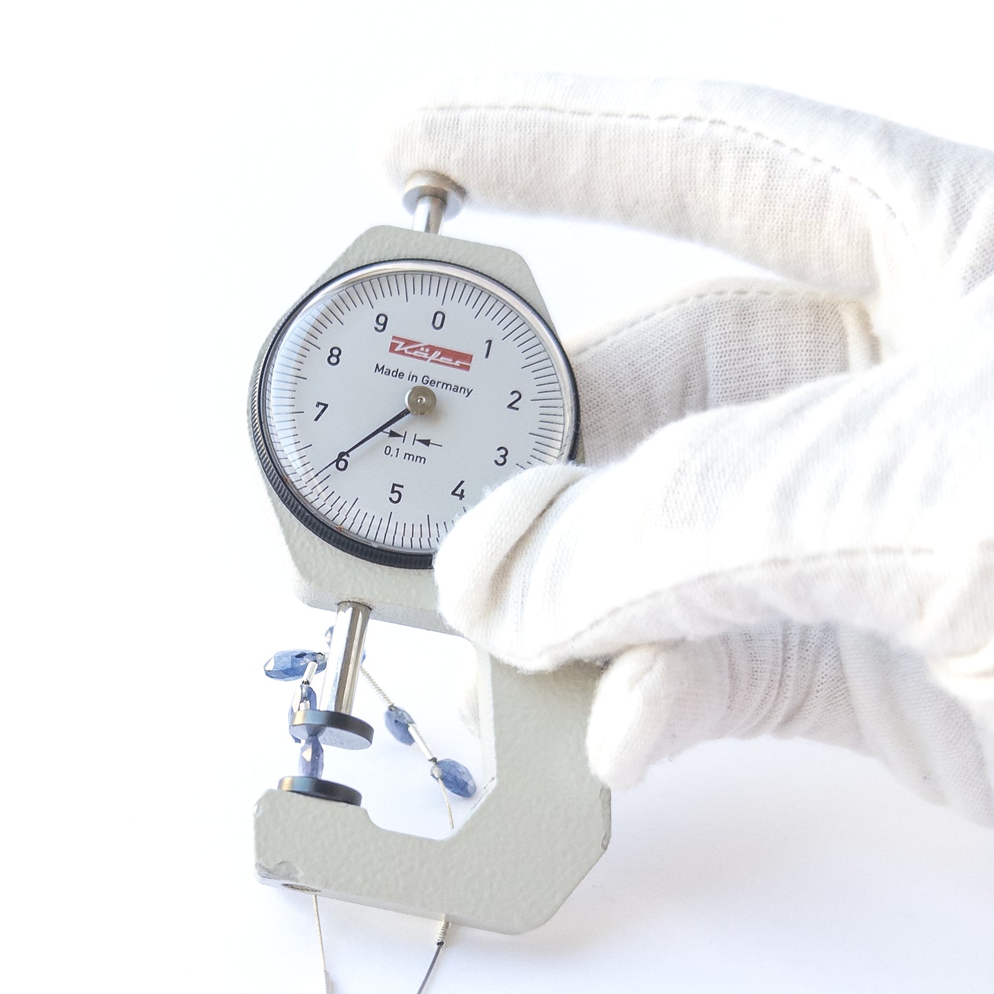 A dial gauge measures the Blue Sapphire faceted briolette 5.2–6.4mm gemstone.