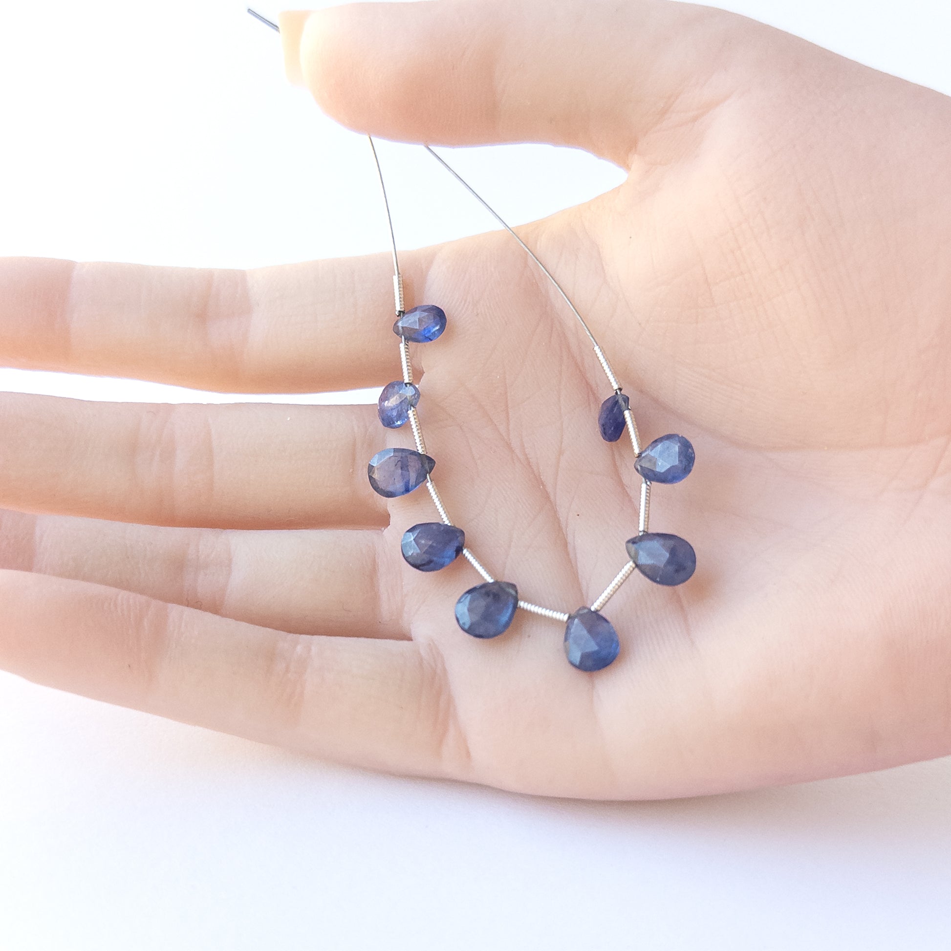 A person holds delicate strands of Blue Sapphire faceted briolette beads, showcasing their cut design.