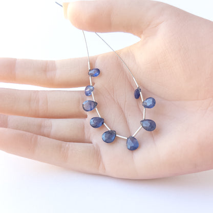 A person holds delicate strands of Blue Sapphire faceted briolette beads, showcasing their cut design.