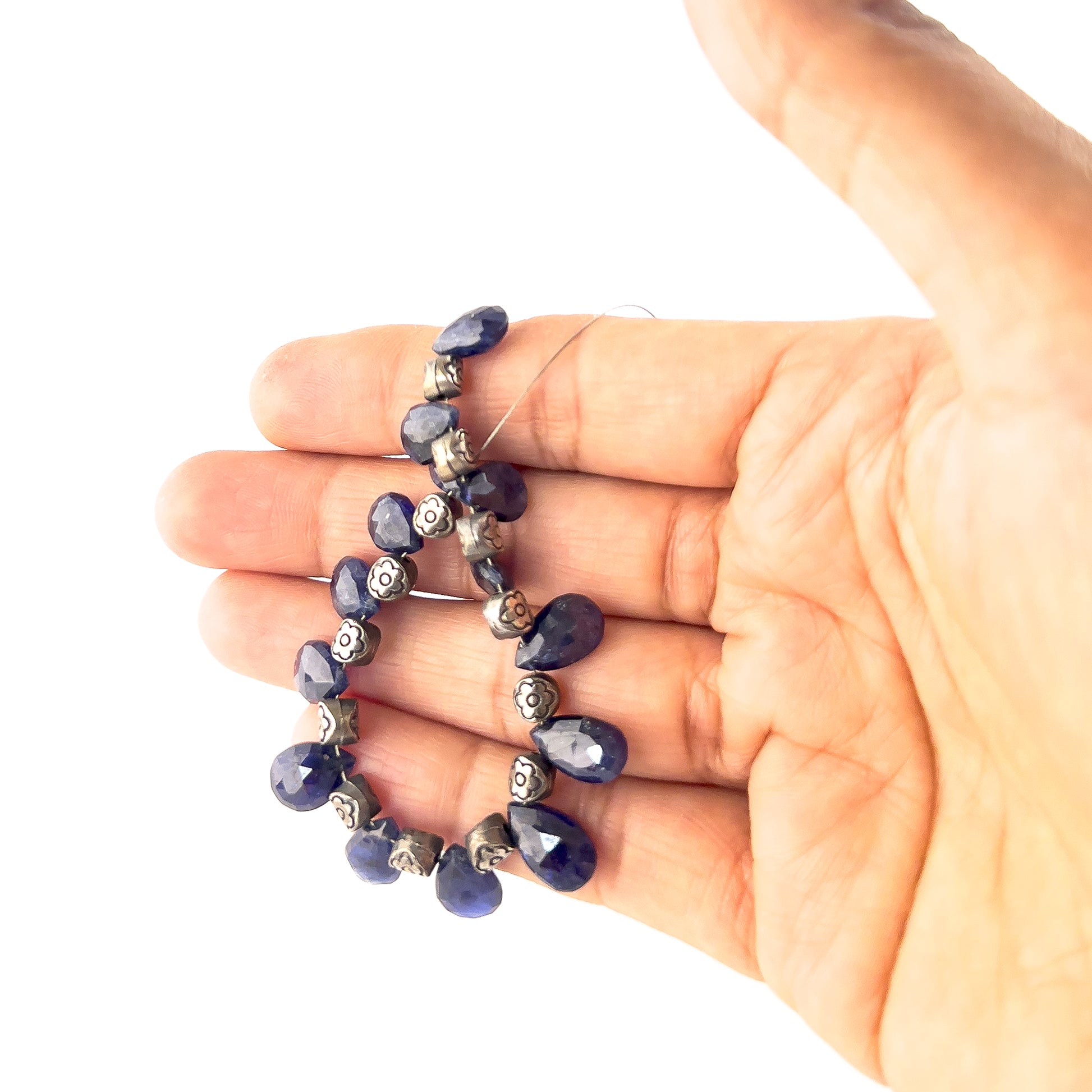 A person holds Blue Sapphire briolette beads, showing their faceted teardrop design and rich blue colour.