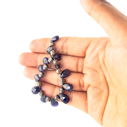 A person holds Blue Sapphire briolette beads, showing their faceted teardrop design and rich blue colour.
