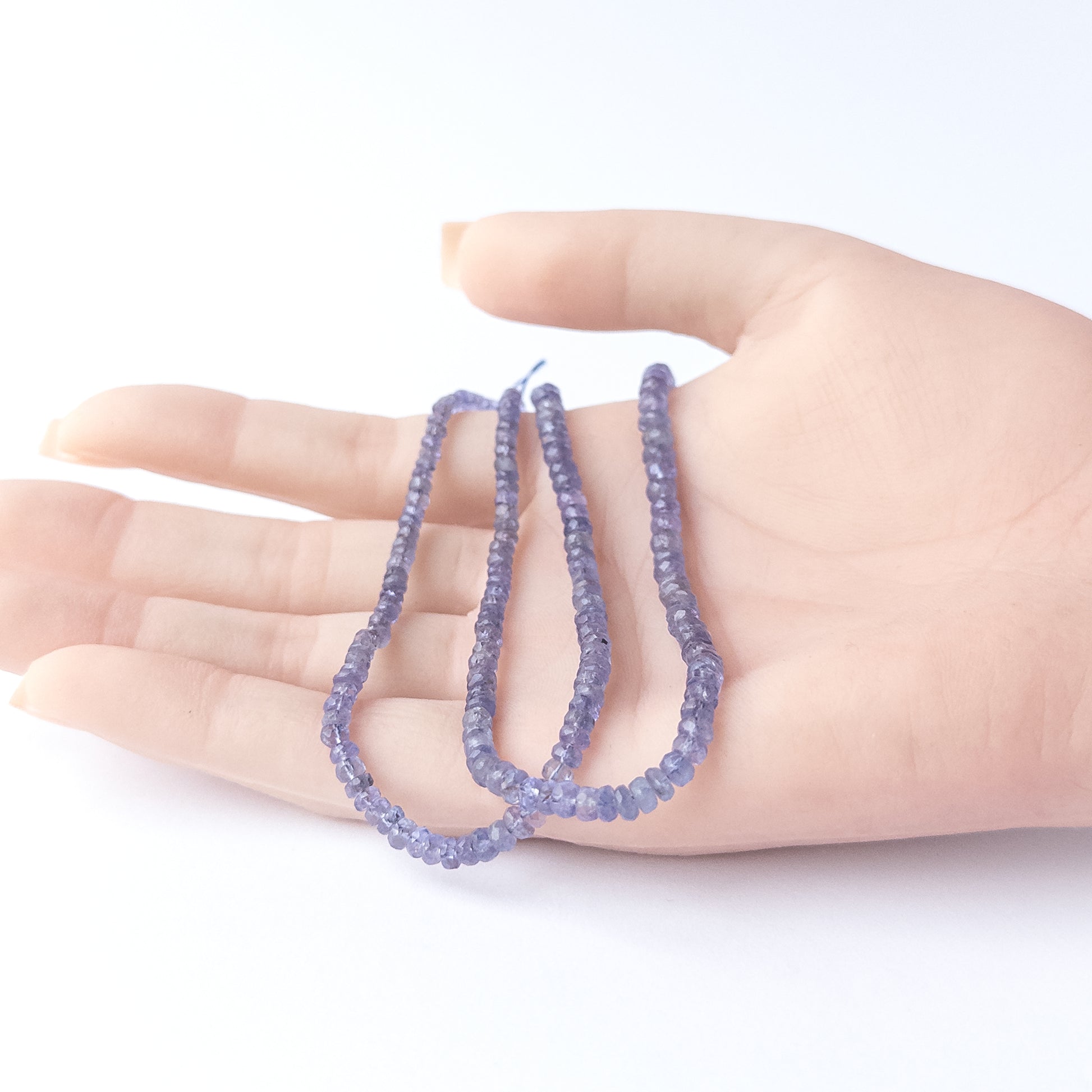 A person holds delicate strands of Blue Sapphire beads, showcasing their faceted rondelle design.