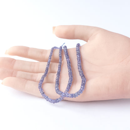 A person holds delicate strands of Blue Sapphire beads, showcasing their faceted rondelle design.