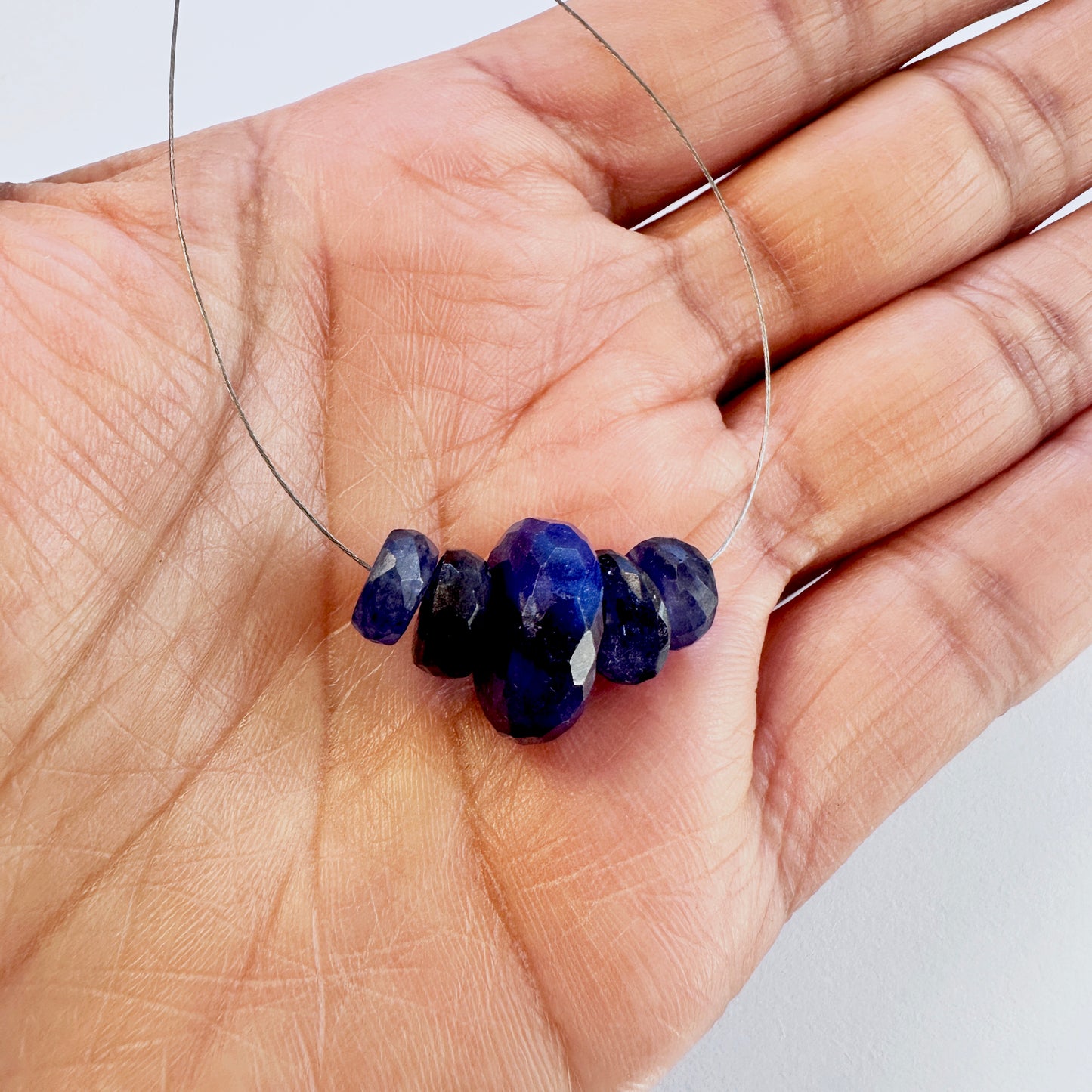 A person holds delicate strands of Blue Sapphire beads, showcasing their smooth design.