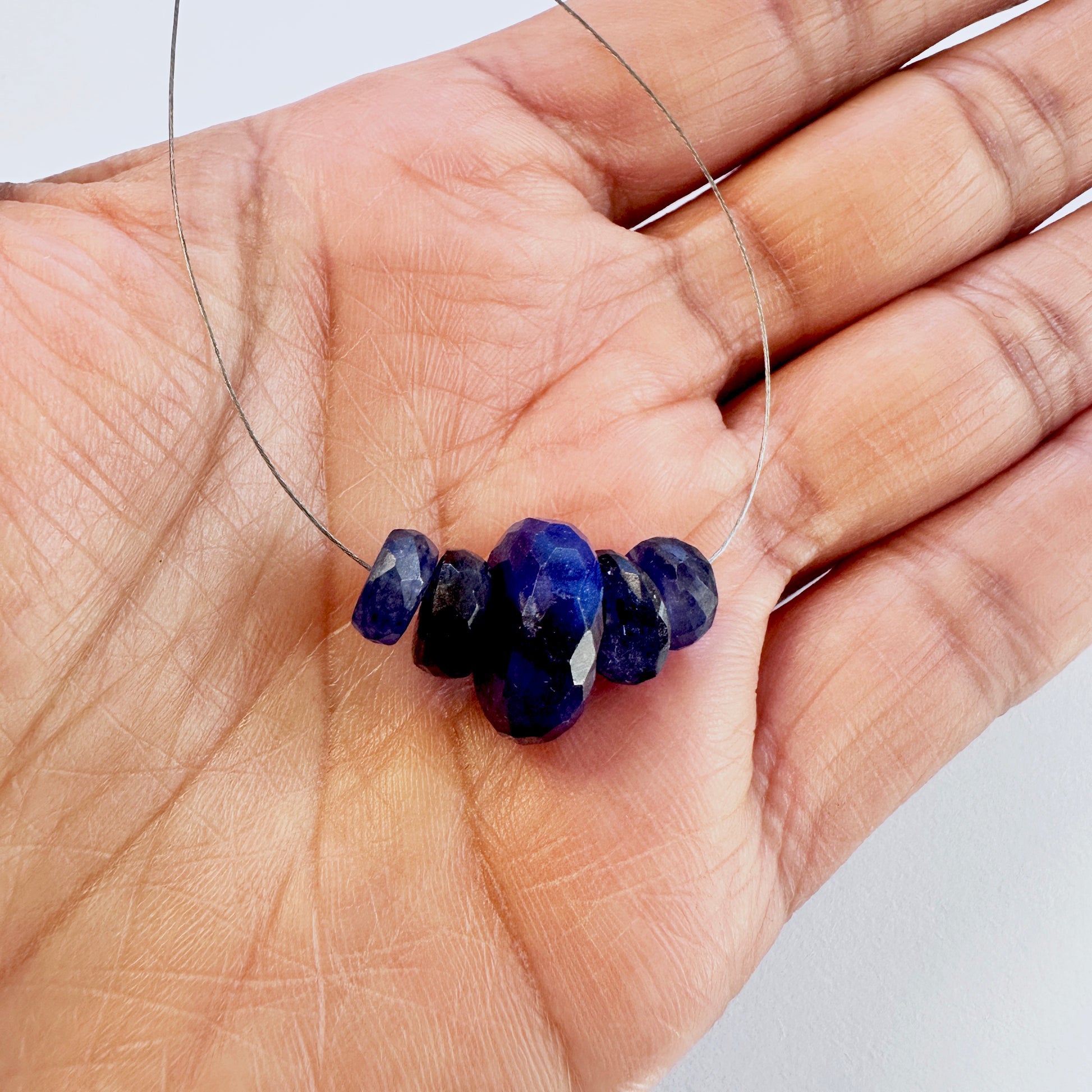 A person holds delicate strands of Blue Sapphire beads, showcasing their smooth design.