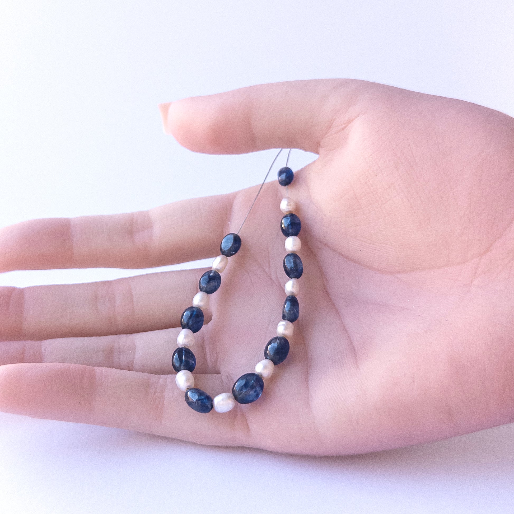 A person holds delicate strands of Blue Sapphire & Freshwater Pearls beads, showcasing their Smooth Oval design.