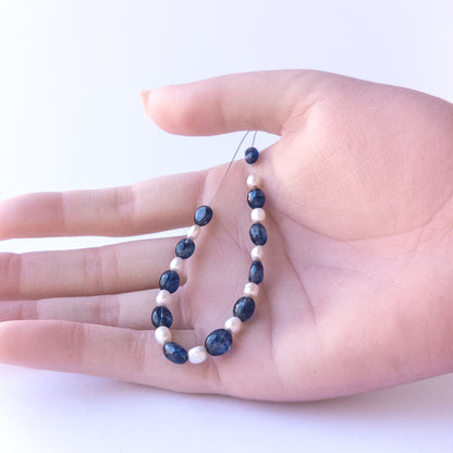 A person holds delicate strands of Blue Sapphire & Freshwater Pearls beads, showcasing their Smooth Oval design.