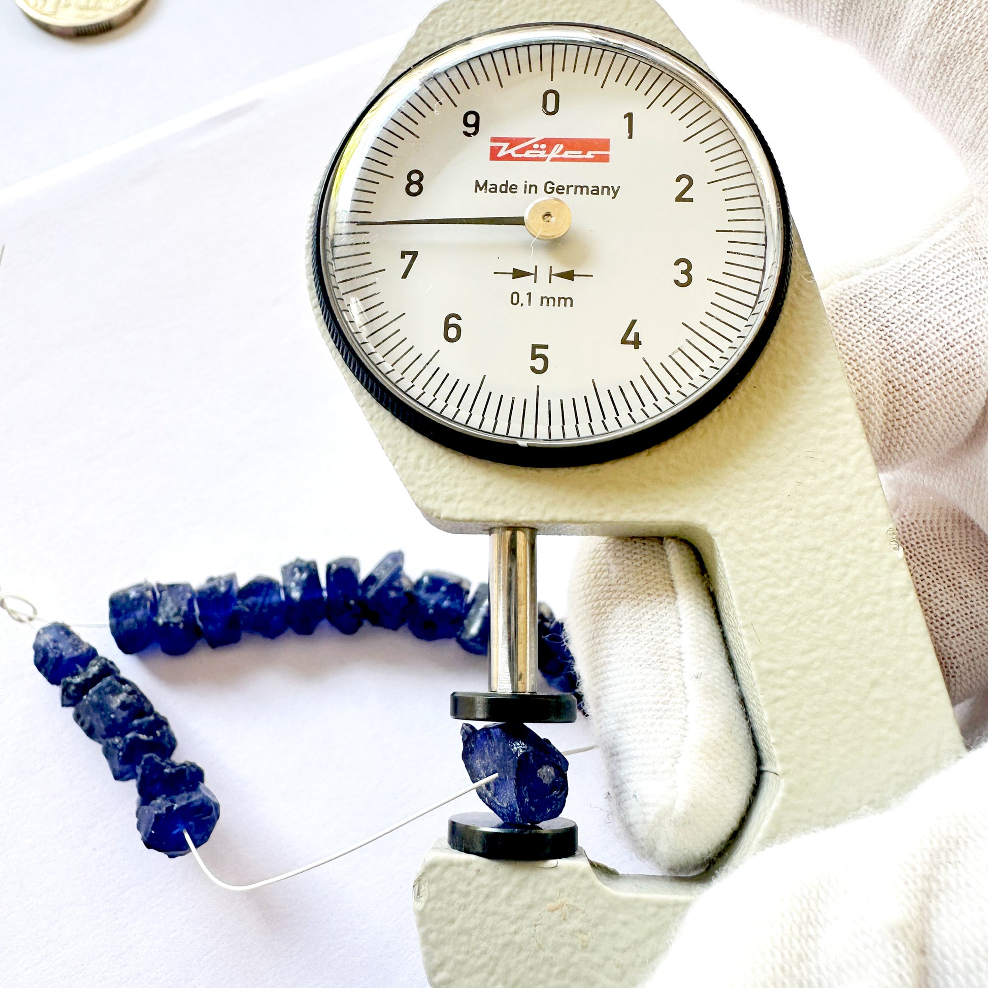 A dial gauge measures the Blue Sapphire rough 6-8mm gemstone bead.