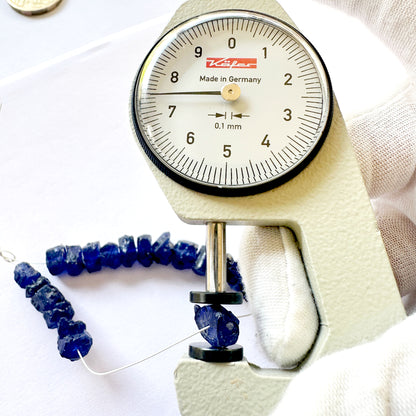 A dial gauge measures the Blue Sapphire rough 6-8mm gemstone bead.