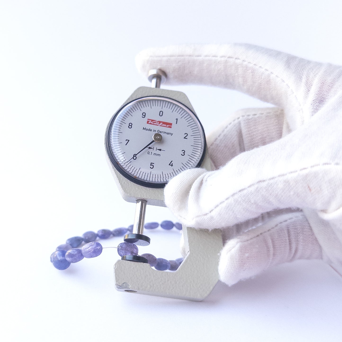 A dial gauge measures the Blue Sapphire smooth oval 4.7–8.2mm gemstone.