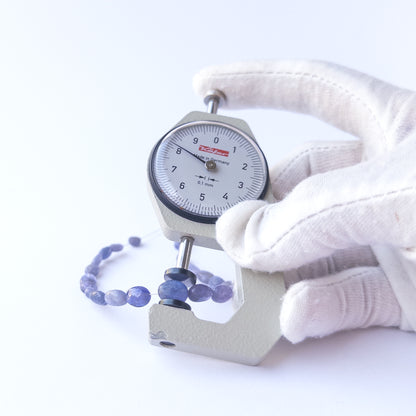 A dial gauge measures the Blue Sapphire smooth oval 4.7–8.2mm gemstone.