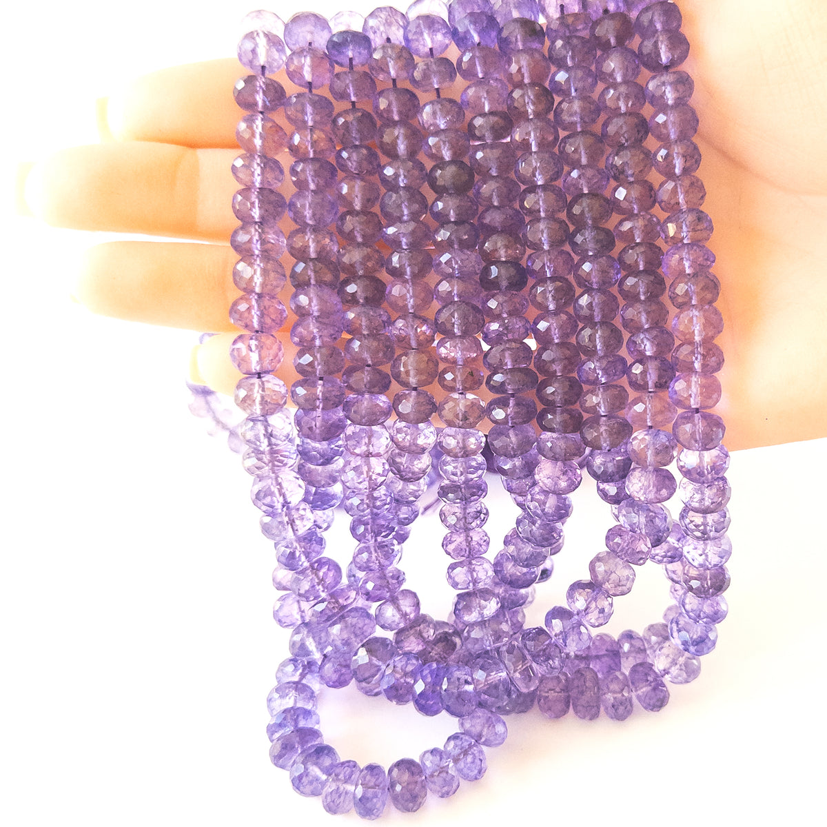A person holds delicate strands of Amethyst beads, showcasing their faceted rondelle design.