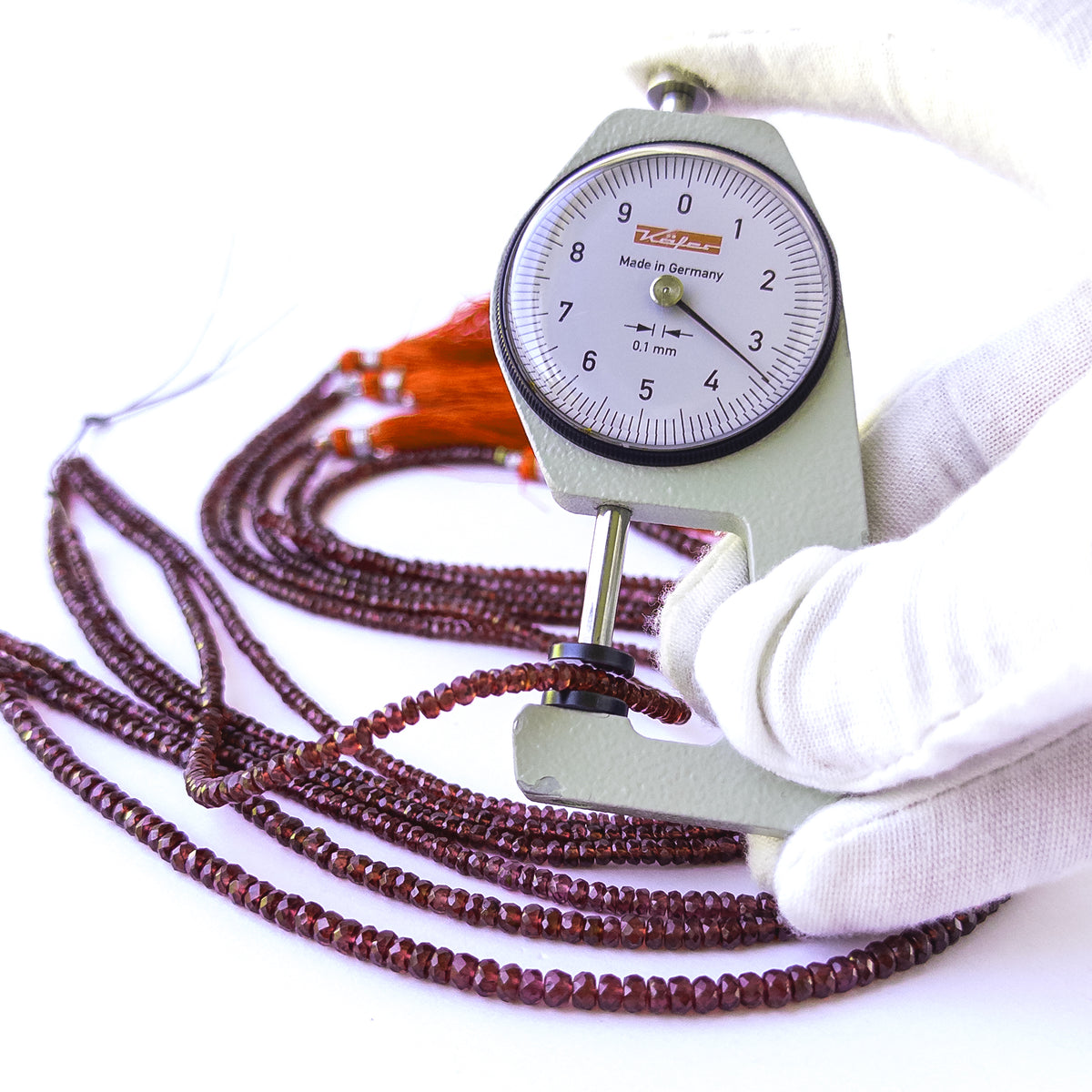A dial gauge measures the Burma Garnet faceted rondelle 3.1–4mm gemstone.