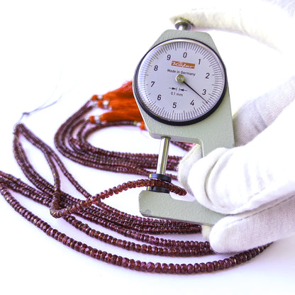 A dial gauge measures the Burma Garnet faceted rondelle 3.1–4mm gemstone.