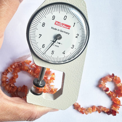 A dial gauge measures the Carnelian chip 5mm to 8mm gemstone, ensuring accuracy in bead sizing.
