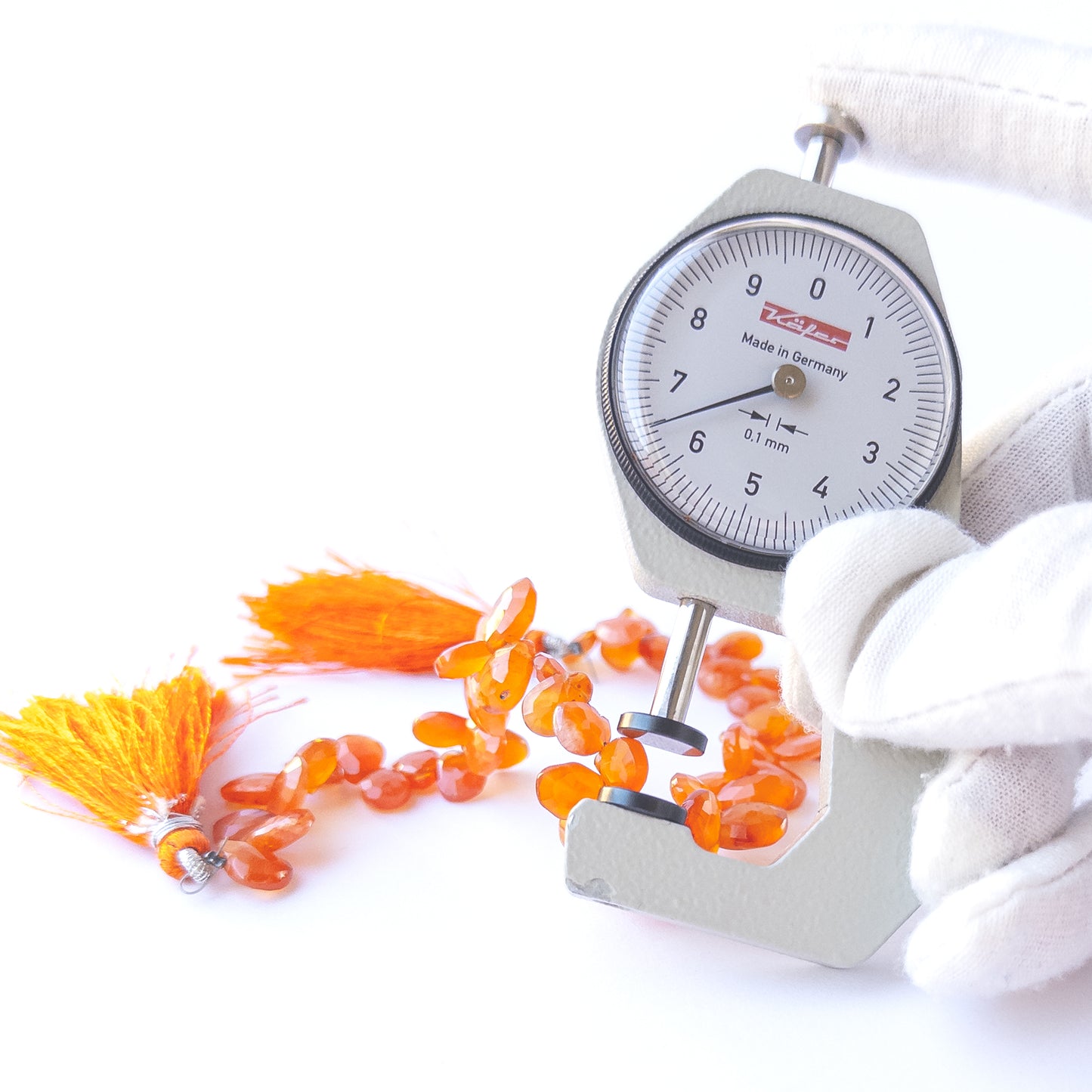 A dial gauge measures the Carnelian faceted briolette 6.7mm gemstone.