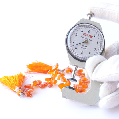 A dial gauge measures the Carnelian faceted briolette 6.7mm gemstone.