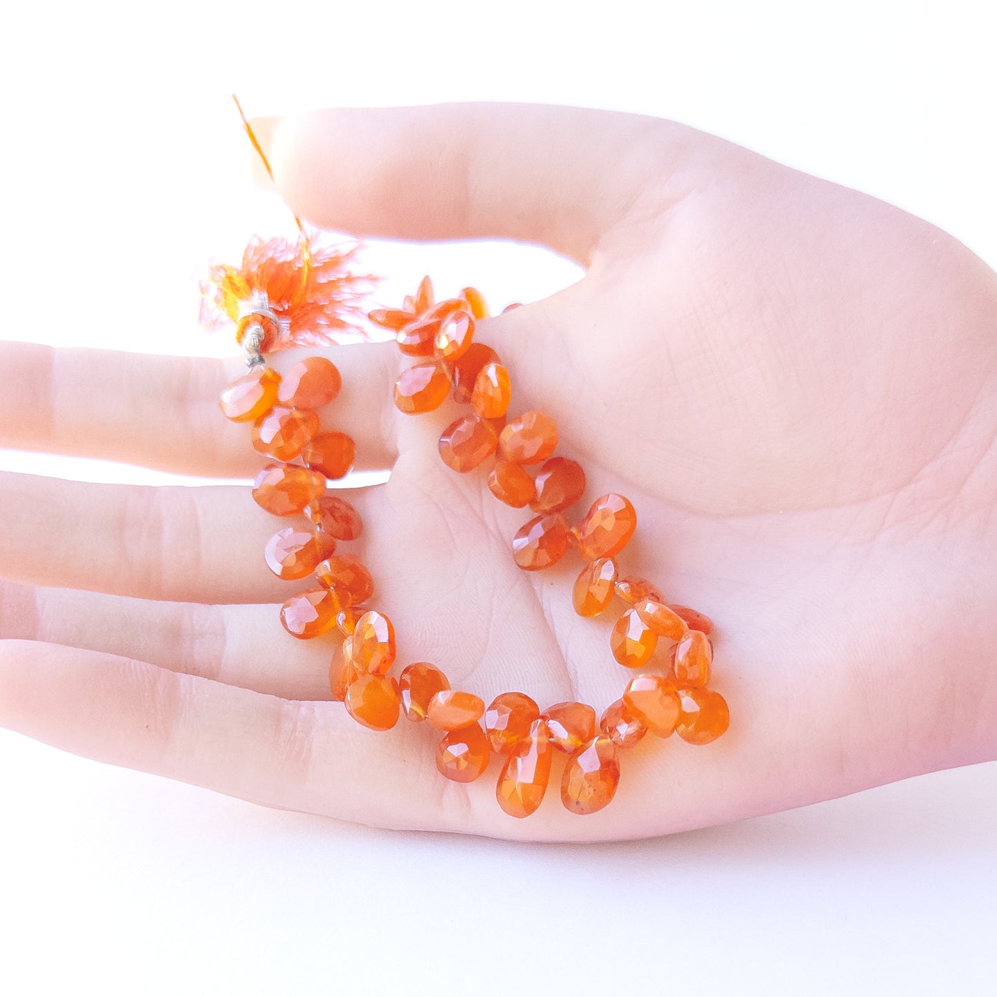 A person holds delicate strands of Carnelian beads, showcasing their faceted briolette design.