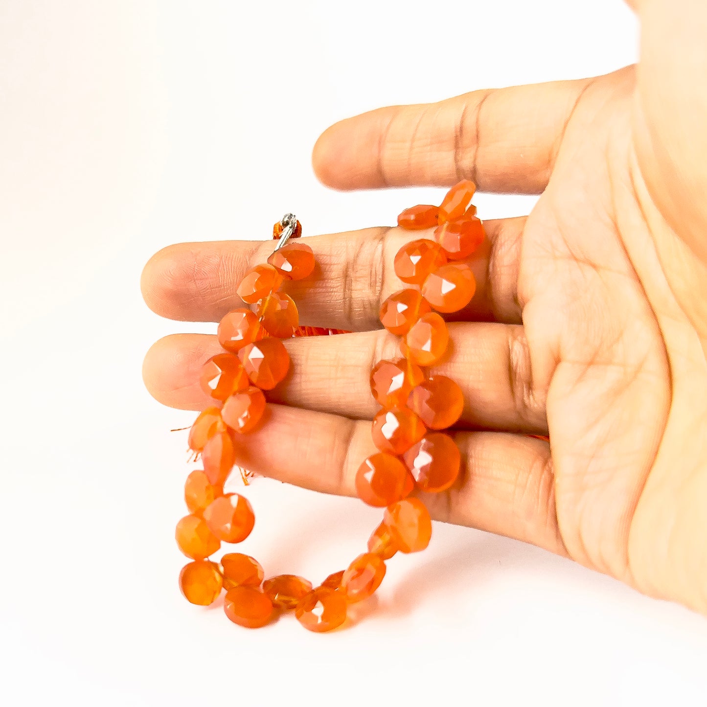 A person holds Carnelian briolette beads, showing their faceted teardrop design and geniune colour.