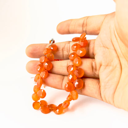 A person holds Carnelian briolette beads, showing their faceted teardrop design and geniune colour.