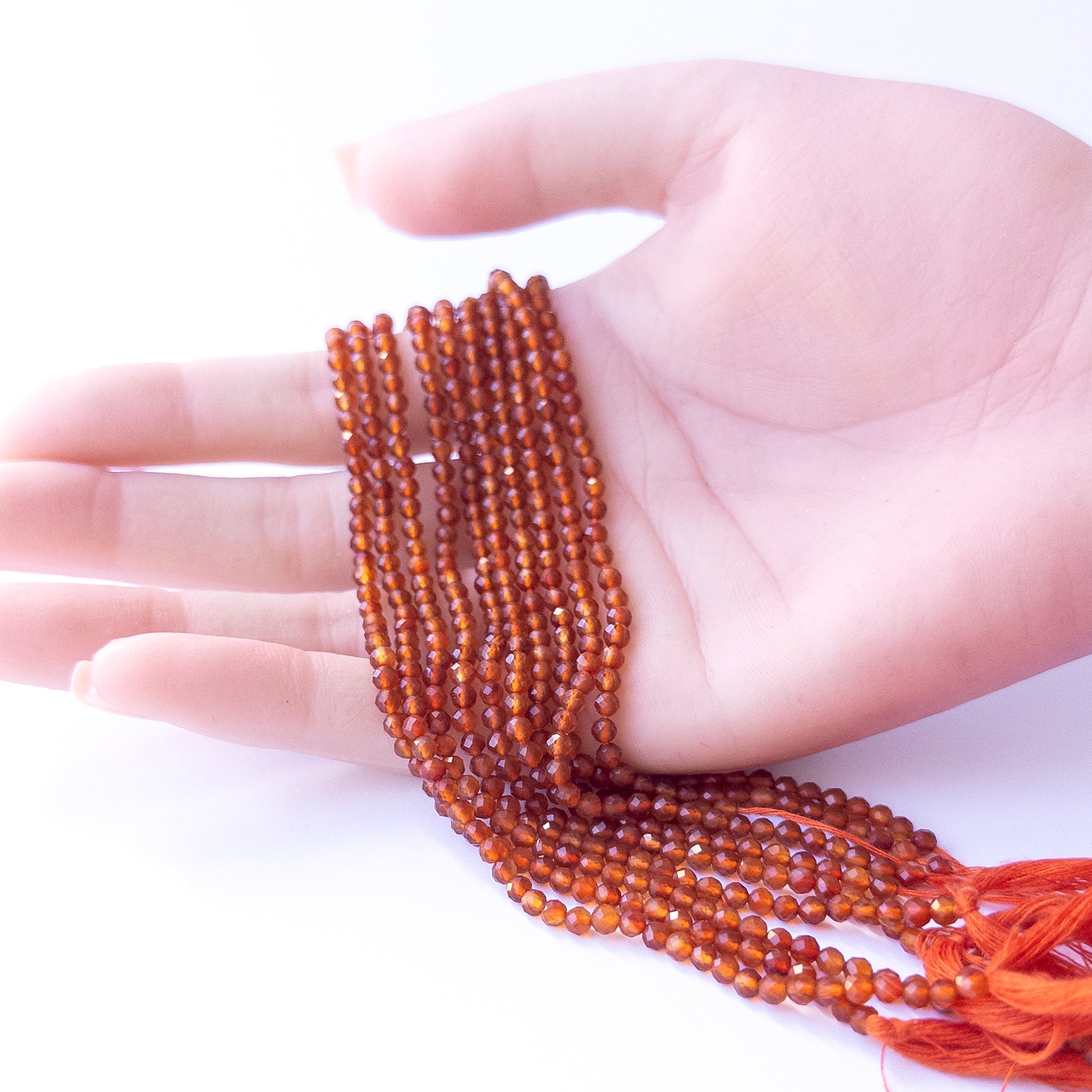 A person holds delicate strands of Carnelian beads, showcasing their faceted rondelle design.