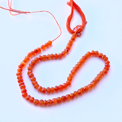 Carnelian faceted rondelle natural gemstone beads in rich orange tones arranged on a 29cm strand for handmade jewellery components.