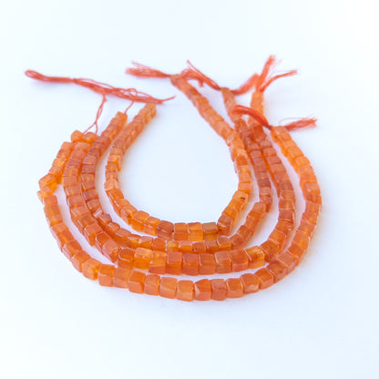 Carnelian smooth cube gemstone beads in 4.8–5.5mm size arranged on a 20cm strand with warm orange shine.