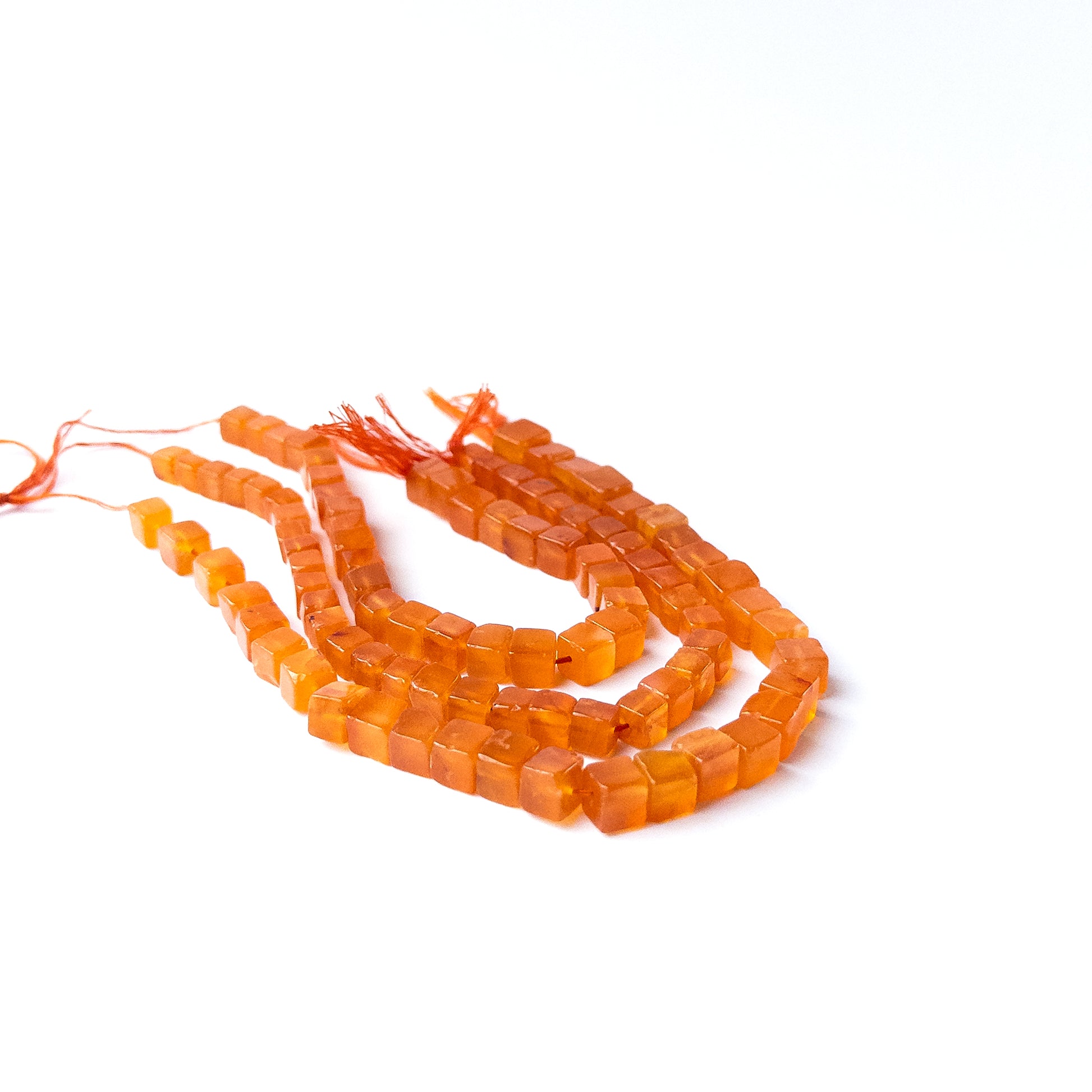 Carnelian smooth cube gemstone beads with warm orange tones arranged neatly for DIY jewellery making.