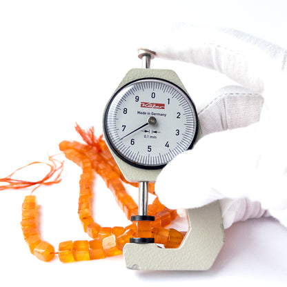 A dial gauge measures the Carnelian smooth cube 5.5–6.5mm gemstone.