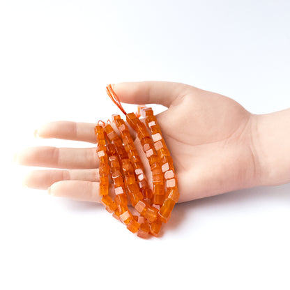 A person holds delicate strands of Carnelian beads, showcasing their smooth cube design.