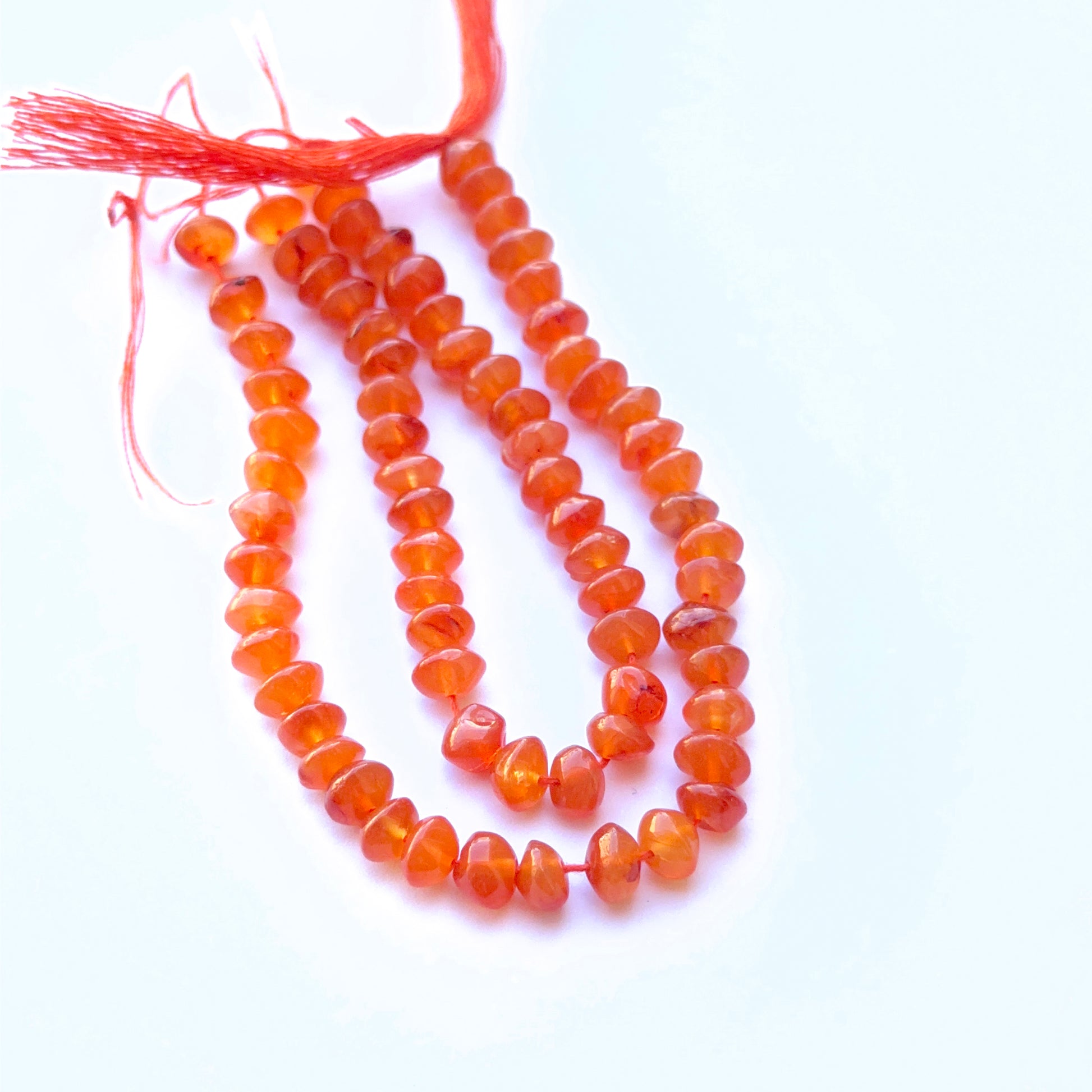 Carnelian smooth rondelle natural gemstone beads in warm orange tones arranged on a 14cm strand for handmade jewellery components.