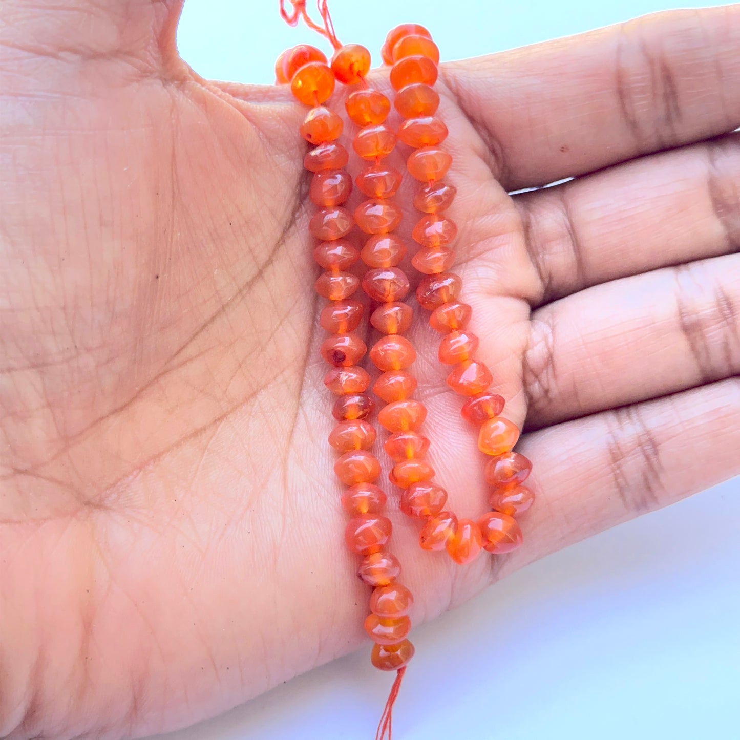 A person holds delicate strands of Carnelian beads, showcasing their smooth design.