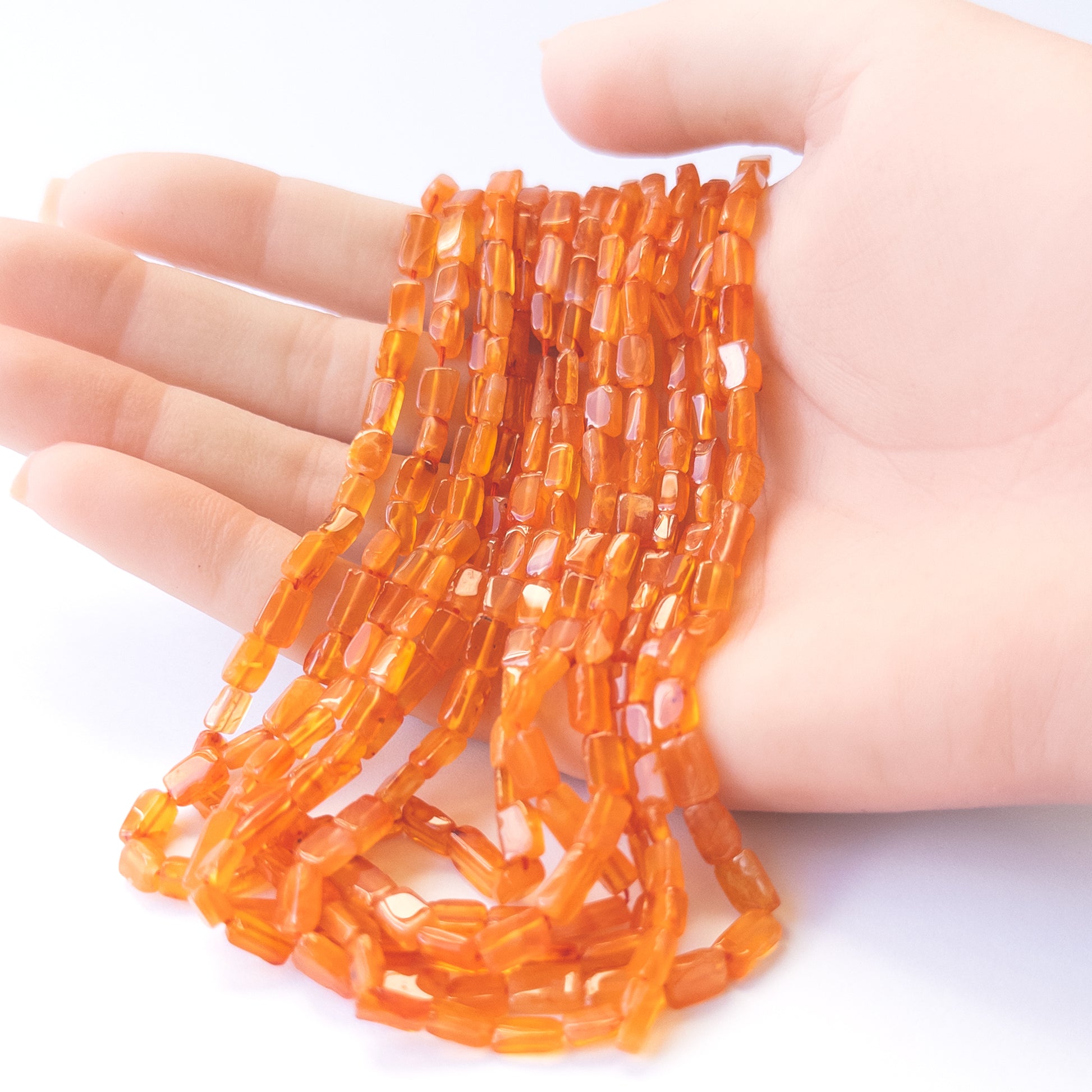 A person holds delicate strands of Carnelian beads, showcasing their smooth rectangle design.