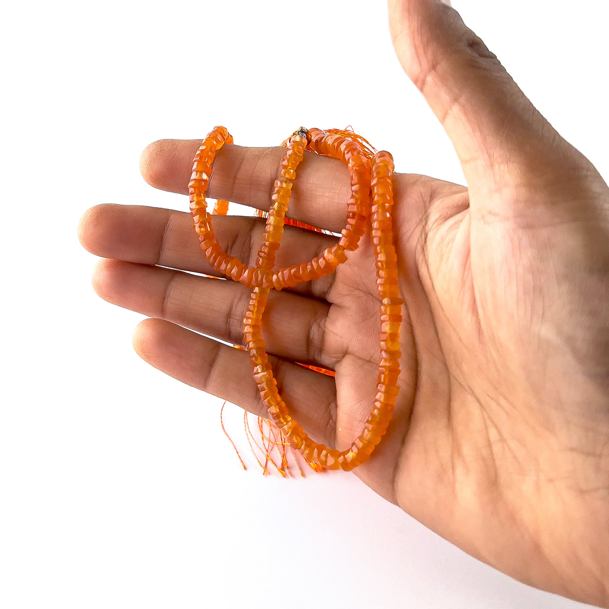 A person holds delicate strands of Carnelian beads, showcasing their smooth wheel heishi design.