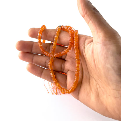 A person holds delicate strands of Carnelian beads, showcasing their smooth wheel heishi design.