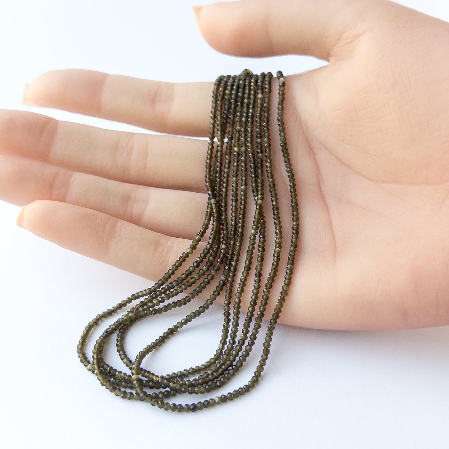 A person holds delicate strands of Cat's Eye beads, showcasing their faceted rondelle design.